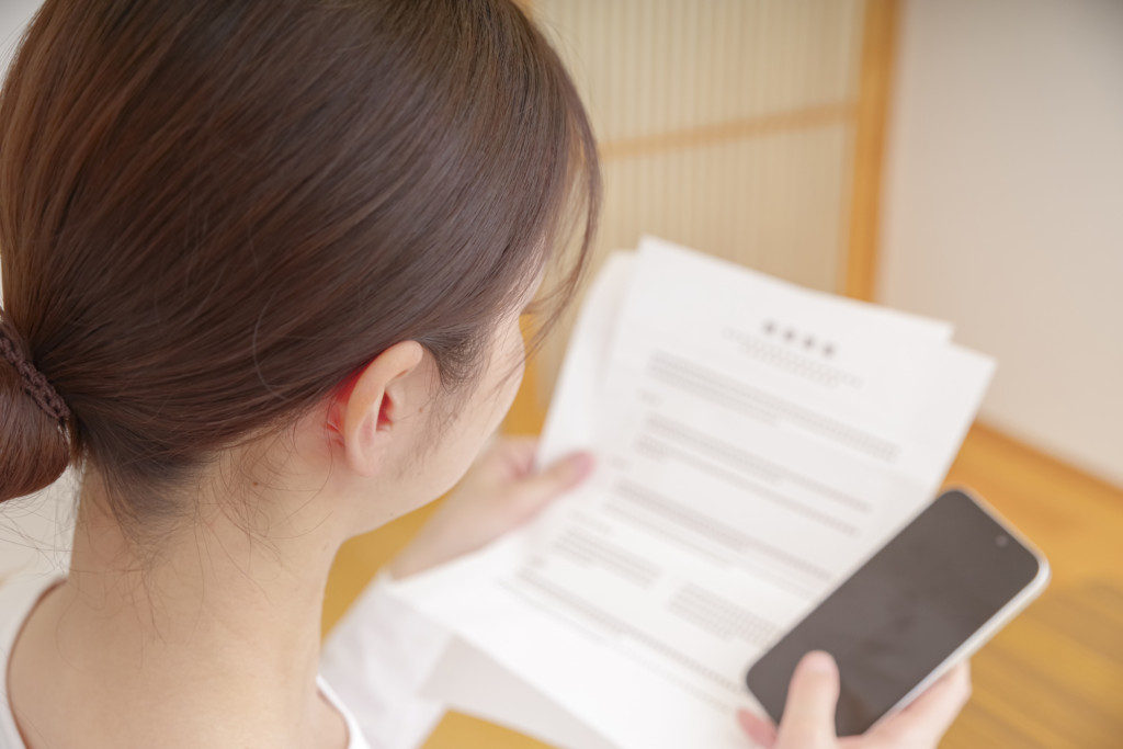 スマホと書類を見つめる女性