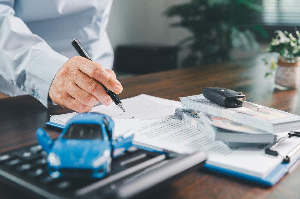 Customer signing insurance document lease agreement table, writing signature contract buying selling new or used vehicle, with car keys, warranty papers, guarantee included in transaction.